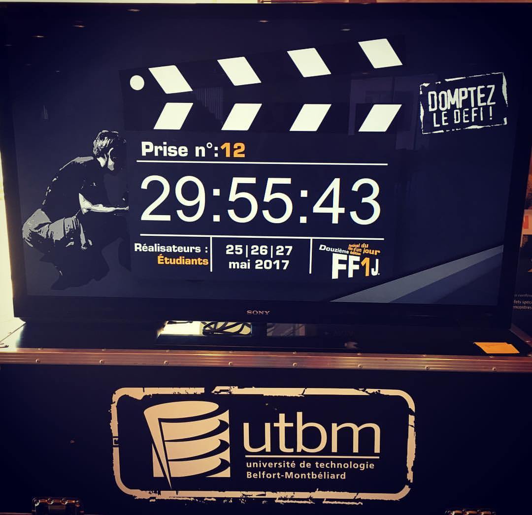 Grand écran de télévision noir (de marque Sony) posé sur une caisse de transport technique (un flight case). L'écran affiche une infographie promotionnelle ou un écran de veille pour un événement cinématographique étudiant organisé par l'UTBM