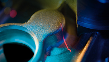 Gros plan macro sur un procédé d'impression 3D métallique ou de frittage laser, montrant un faisceau laser rouge frappant une surface de poudre texturée sous un éclairage bleu