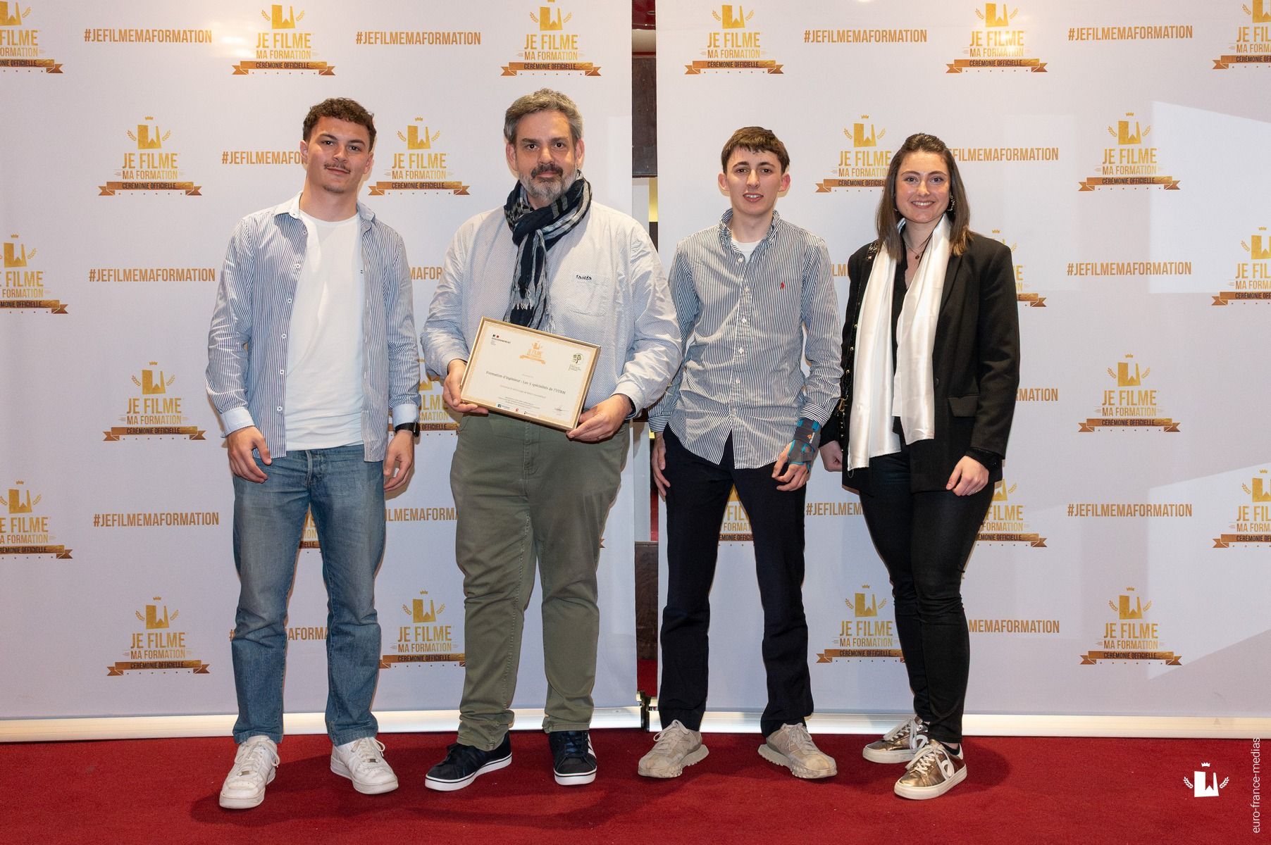 Quatre personnes debout sur un tapis rouge, posant pour une photo officielle lors de la cérémonie "JE FILME MA FORMATION".