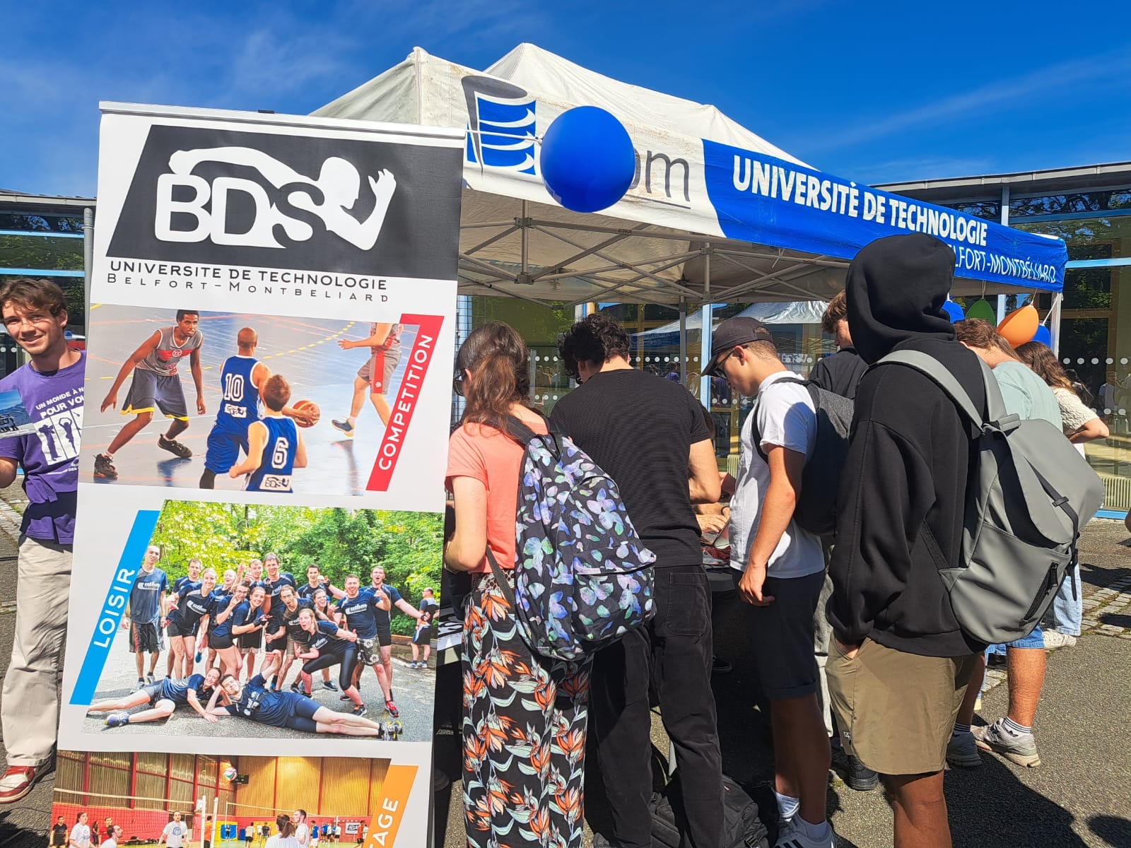 un groupe d'étudiants à l'extérieur, regardant le stand du bureau des sports