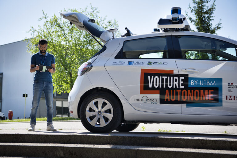 Une vue d'une voiture autonome by UTBM. Un ingénieur se trouve derrière elle avec une tablette à la main