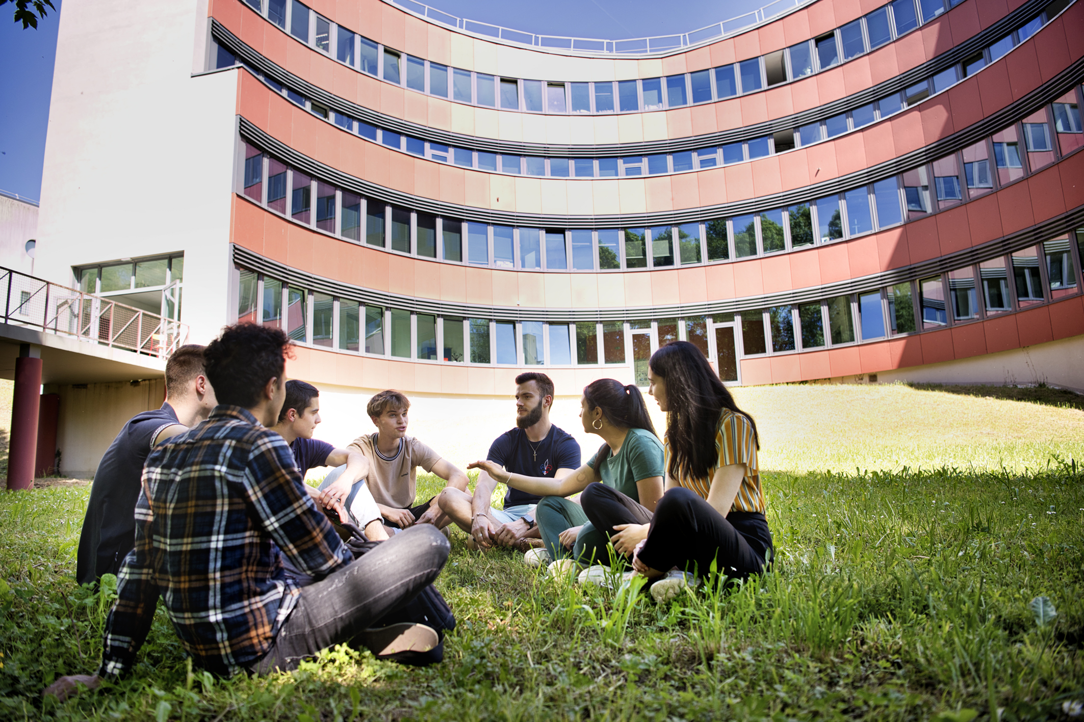 Un groupe d'étudiants assis dans l'herbe, derrière l'un des batiments UTBM de Sevenans
