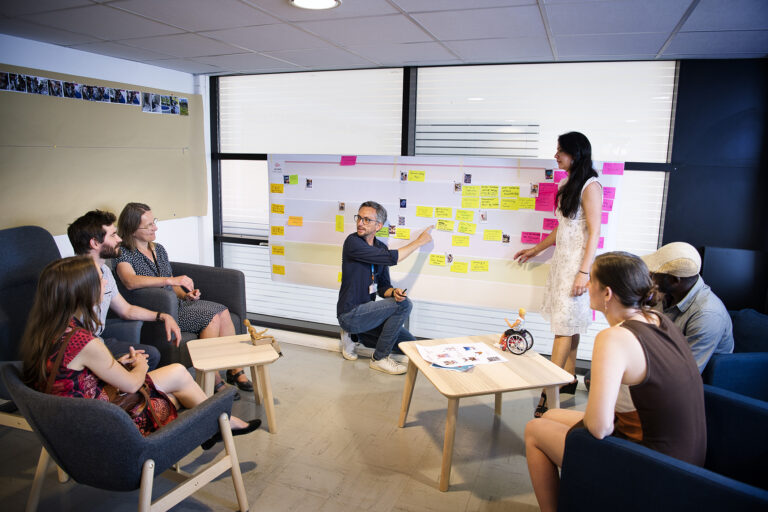 Cinq personnes assistent à une présentation d'un projet, présenté par un homme et une femme