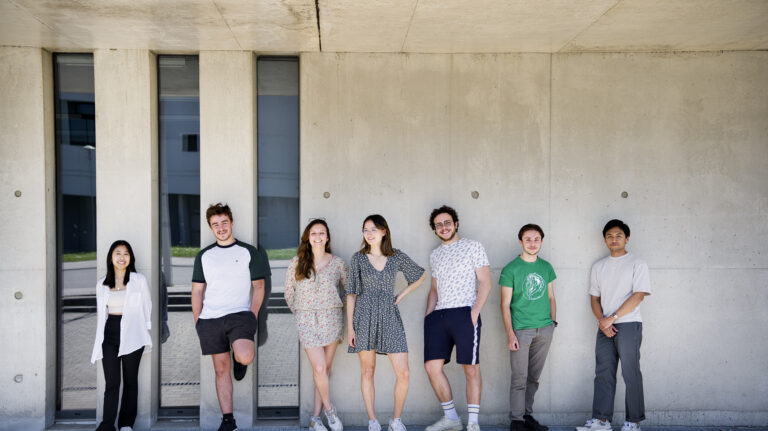 Photo de groupe d'étudiants en extérieur adossés à un batiment vitré