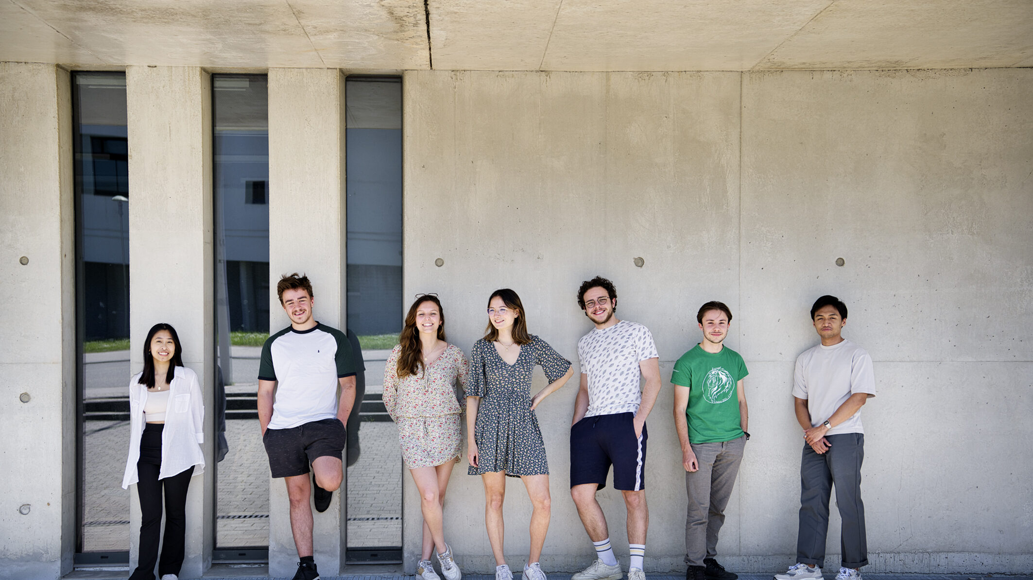 Photo de groupe d'étudiants en extérieur adossés à un batiment vitré